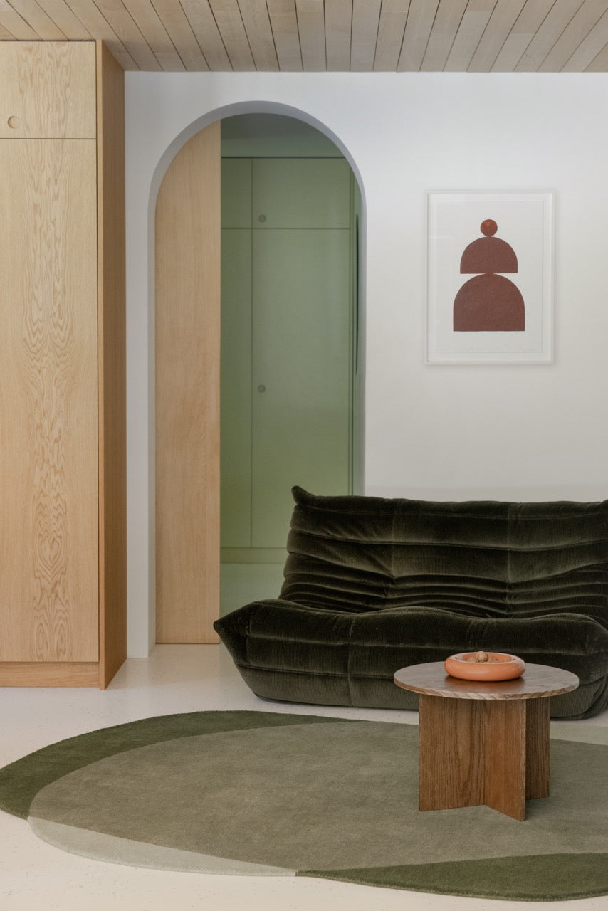 Abstract hand-tufted rug in forest and olive tones beneath oak coffee table